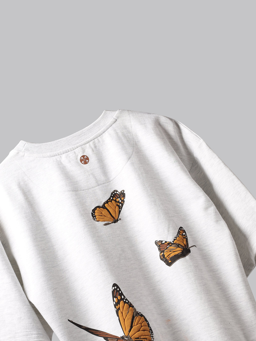 Back side of White orange butterflies oversized t-shirt on a grey background.