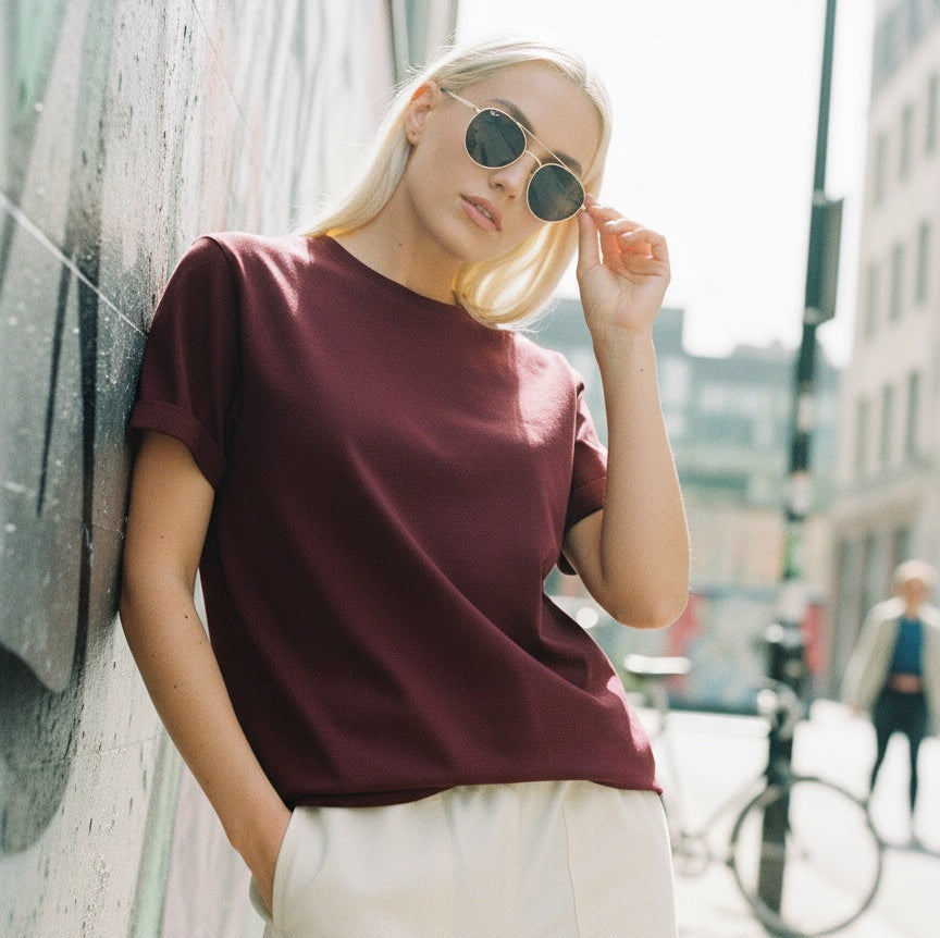 Person wearing a jayhues basic burgundy t-shirt, standing against a wall on a city street.