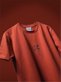 A rust colored t-shirt with a small dark black hd printed logo mark on the chest, displayed against a matching dark reddish-brown background.