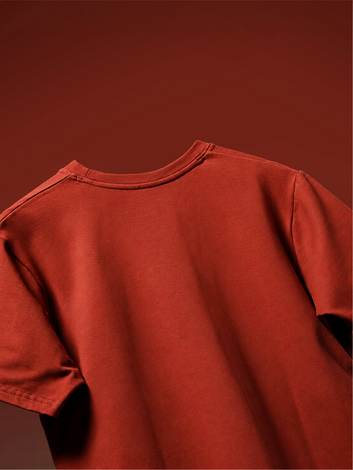 A close-up of a rust t-shirt from back showing the back neckline and shoulder seams, set against a matching solid rust-red background.