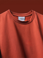 A close-up of the rust basic t-shirt, set against a matching rust-orange background.