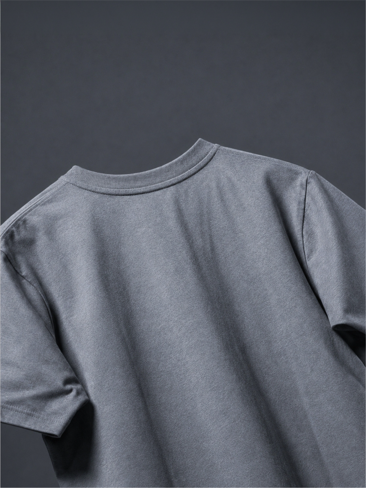 Close-up of the back of the grey basic t-shirt against a dark gray background.