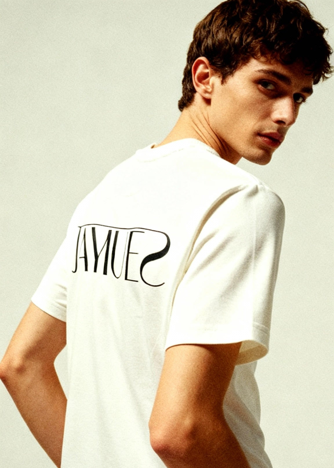 Man wearing a white t-shirt with 'jayhues' branding in the back side of shirt, on a light background